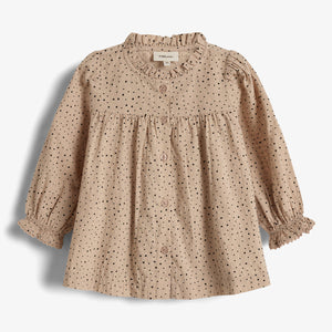 Bluse mit Punkten, hängt unverändert; Umgebung ist einfarbiger Hintergrund. Text auf Schild: "Manufacture 9-12M".