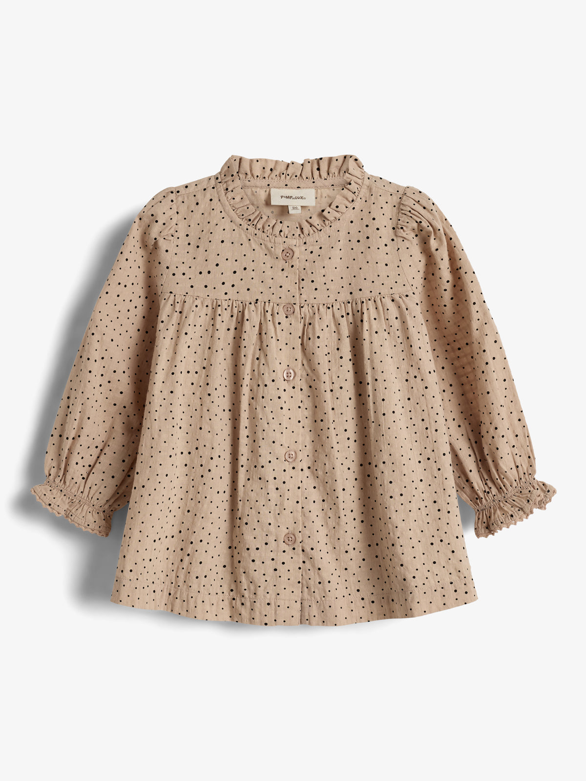 Bluse mit Punkten, hängt unverändert; Umgebung ist einfarbiger Hintergrund. Text auf Schild: "Manufacture 9-12M".