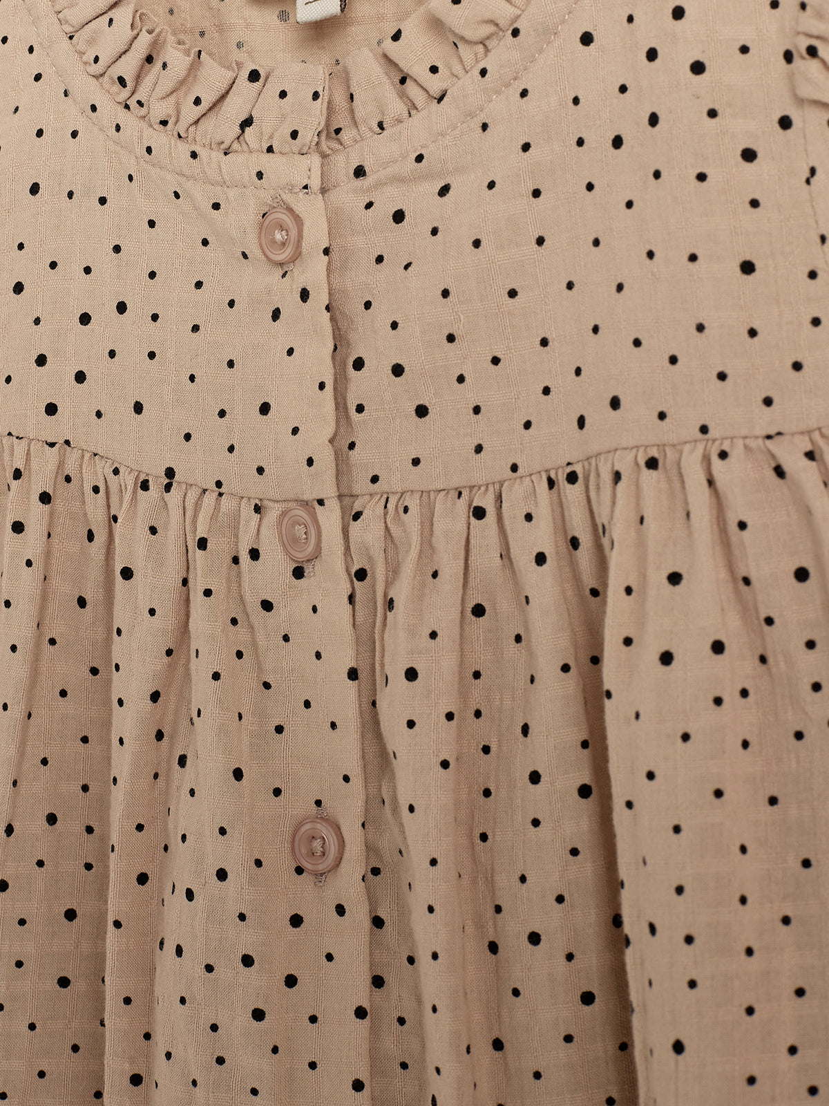 Ein beige Kleid mit schwarzen Punkten und Rüschenkragen ist im Bild zu sehen. Es hat eine Knopfleiste mit drei Knöpfen.