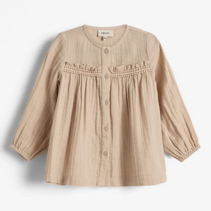 Beige Kinderbluse mit Knöpfen und Rüschen, aus leichtem Stoff gefertigt. Das Etikett zeigt „pure love“ und „38“. Die Bluse liegt vor einem weißen Hintergrund.