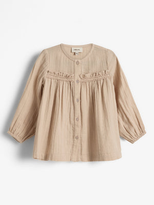 Beige Kinderbluse mit Knöpfen und Rüschen, aus leichtem Stoff gefertigt. Das Etikett zeigt „pure love“ und „38“. Die Bluse liegt vor einem weißen Hintergrund.