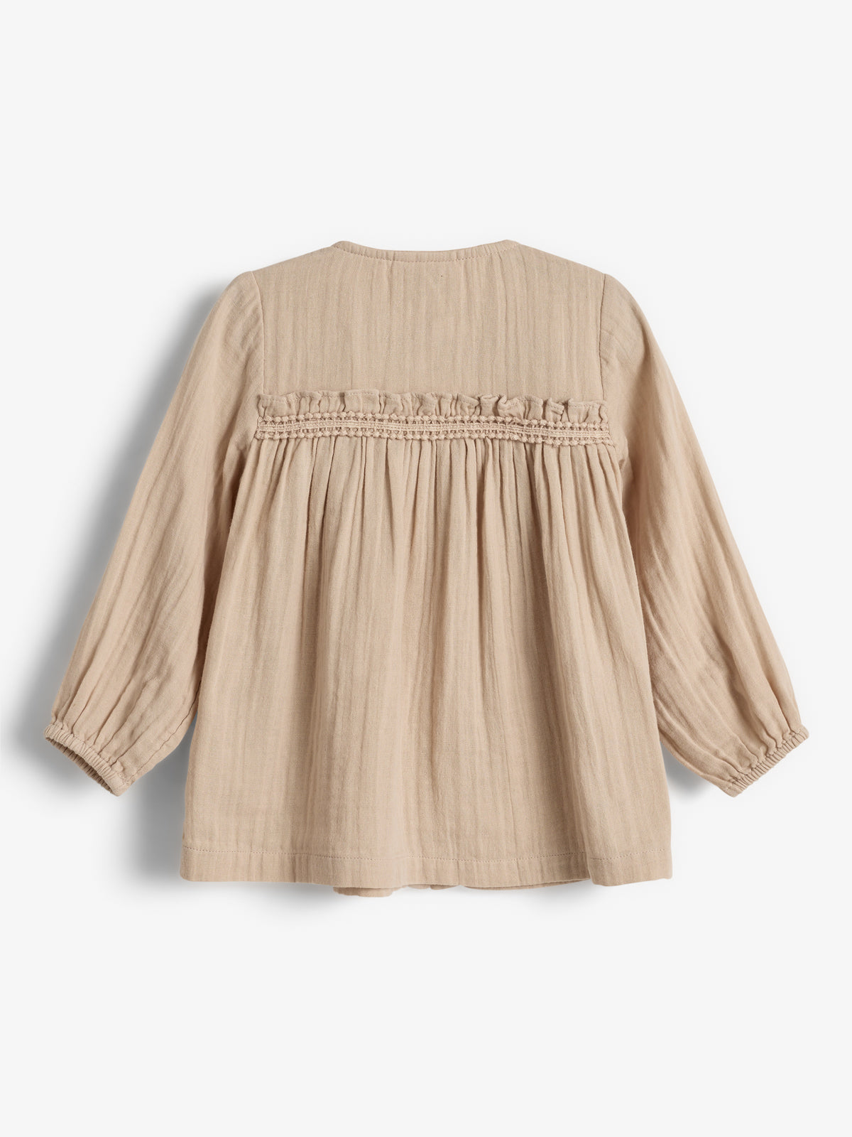 Eine beige Kinderbluse ist ausgestellt aus leichtem Stoff, hat lange Ärmel mit gerafftem Stoff und befindet sich vor einem weißen Hintergrund.