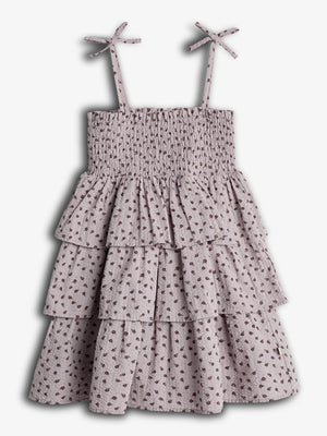 Ein ärmelloses Sommerkleid mit schmalen Trägern und Rüschen, dekoriert mit kleinen Blumenmustern, hängt an einem neutralen Hintergrund.