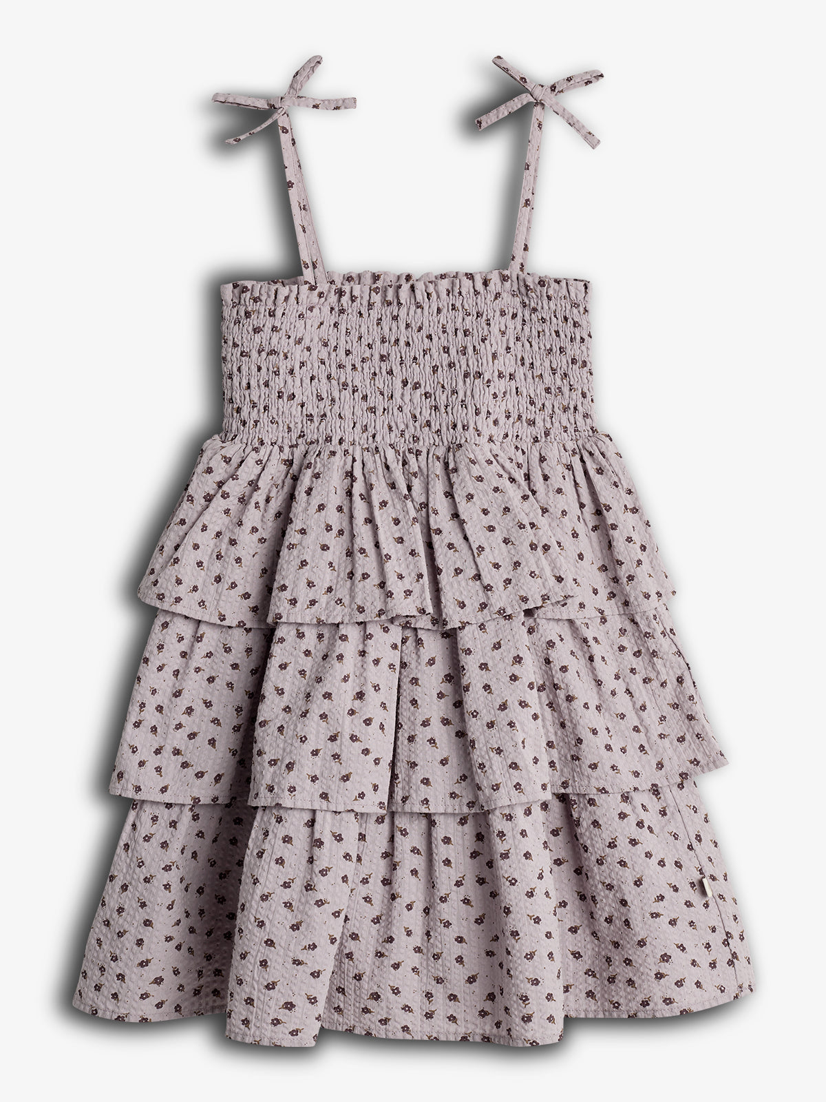 Ein ärmelloses Sommerkleid mit schmalen Trägern und Rüschen, dekoriert mit kleinen Blumenmustern, hängt an einem neutralen Hintergrund.