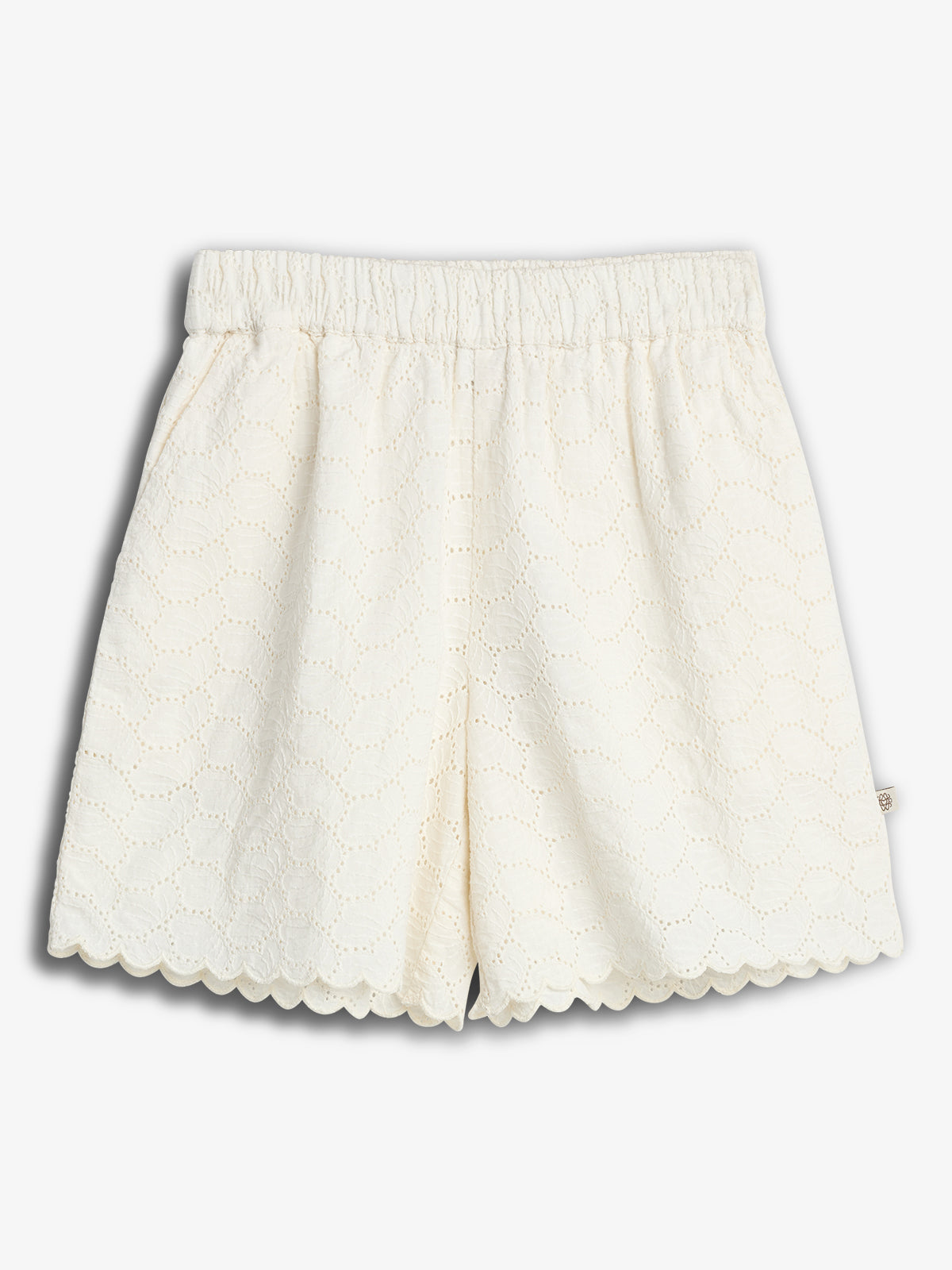 Weiße Shorts mit Broderie-Anglaise-Muster, elastischem Bund und wellenförmigem Saum, präsentiert auf weißem Hintergrund.