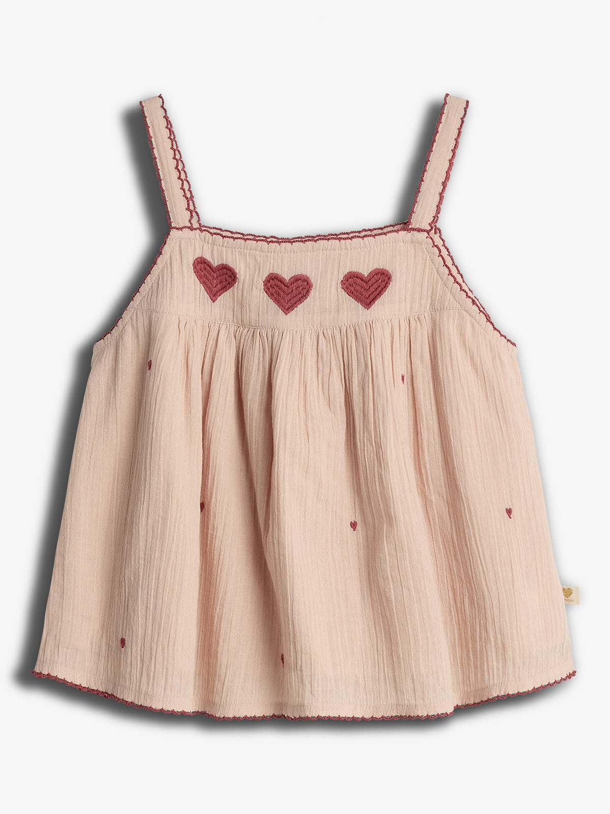 Ein ärmelloses, beigefarbenes Top mit roten Herzstickereien entlang des Dekolletés, umgeben von minimal eingeritzten Herzmotiven und zarten, rot umsäumten Trägern.