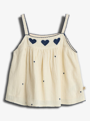 Ein cremefarbenes Kinderträgertop mit dunkelblauen herzförmigen Stickereien entlang des Brustbereichs. Die Träger sind mit blauen Details verziert. Es liegt auf einem weißen Hintergrund.