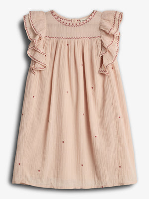 Ein rosa Kinderkleid mit roten Stickereien und Herzmustern ziert die ausgestellten Schultern. Es hängt vor einem neutralen, weißen Hintergrund.