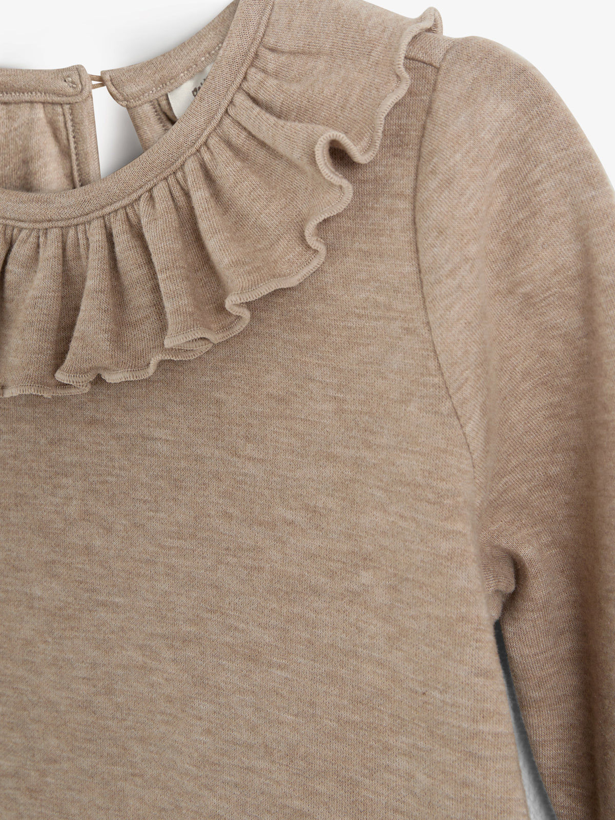 Beiger Pullover mit Rüschenkragen, hängt still. Der Stoff ist weich und strickartig, zeigt fein gewebtes Muster. Hintergrund ist schlicht weiß.