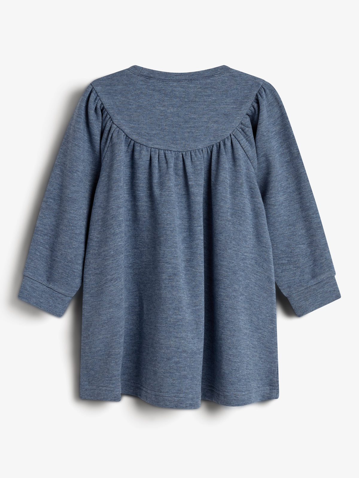 Langärmliges, blaues Kinderkleid hängt regungslos vor weißem Hintergrund. Der Stoff hat eine Raffung am oberen Rückenbereich und weitet sich nach unten hin.