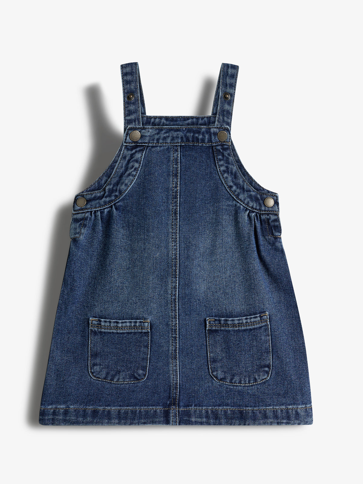 Jeanskleid mit Trägern und vier Knöpfen. Es hat zwei aufgesetzte Taschen vorne. Der Stoff ist dunkelblau, leicht verwaschen. Hintergrund ist ein neutraler, heller Ton.