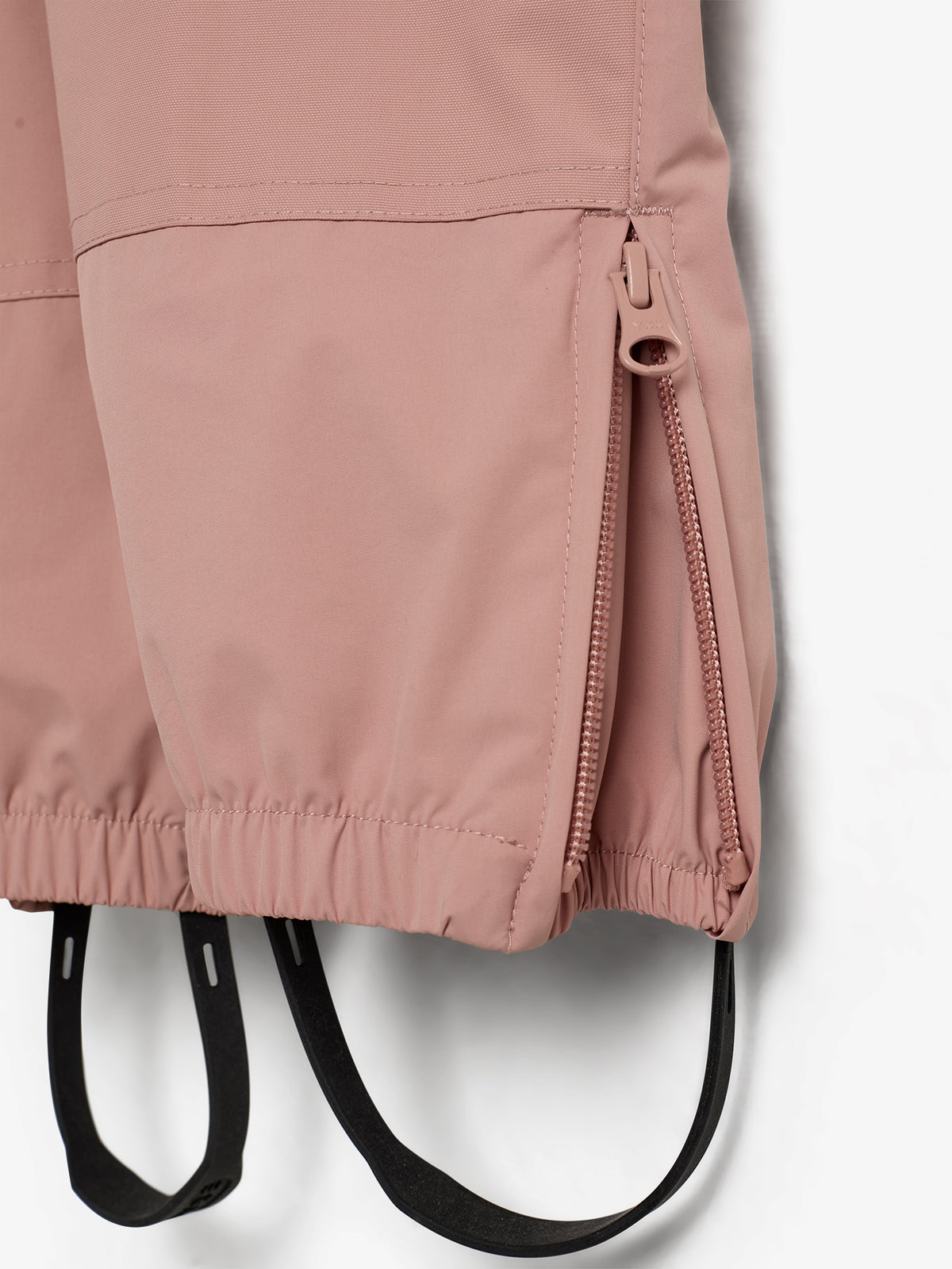 Rosa Jacke mit Reißverschluss, teilweise geöffnet. Elastische Bündchen und schwarze Riemen hängen unten. Der Hintergrund ist neutral und schlicht.