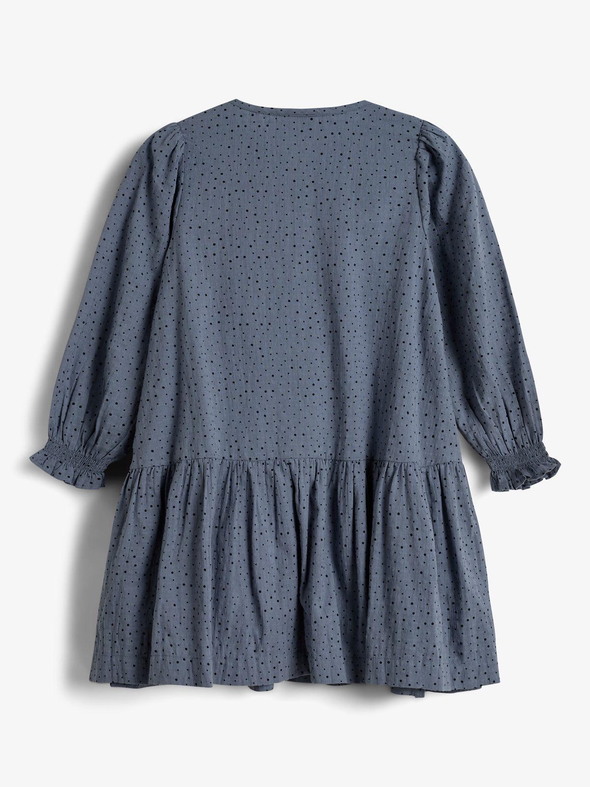 Kleid in Dunkelblau mit kleinen schwarzen Punkten, langen Ärmeln und Rüschen unter der Taille; hängt in einem weißen, leeren Hintergrund.
