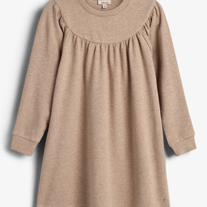 Ein beigefarbenes Kleid mit langen Ärmeln hängt vor einem neutralen Hintergrund. Der obere Teil ist leicht gerafft, und es hat einen runden Ausschnitt.