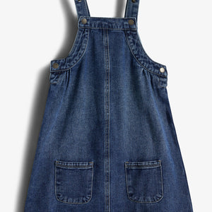 Jeanskleid mit zwei Trägern, Knöpfen und aufgesetzten Taschen, liegt flach auf einem weißen Hintergrund.