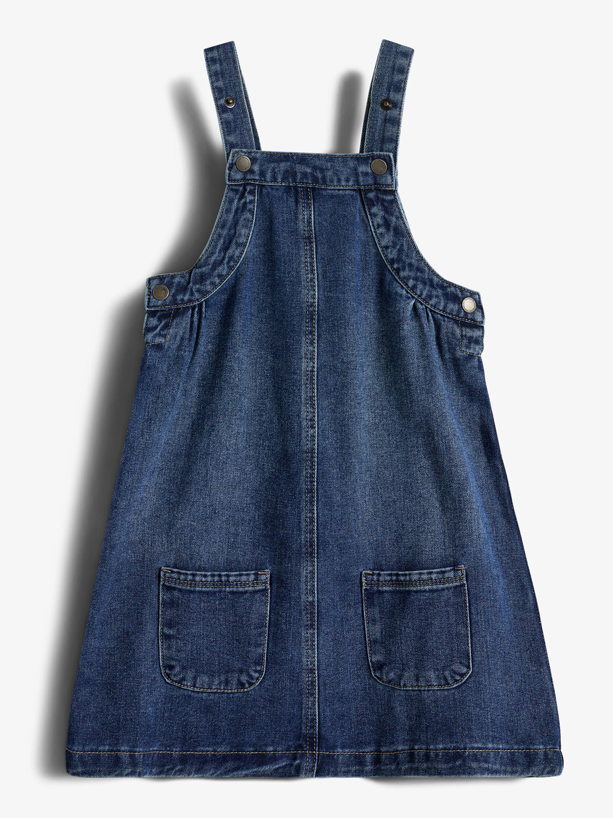 Jeanskleid mit zwei Trägern, Knöpfen und aufgesetzten Taschen, liegt flach auf einem weißen Hintergrund.