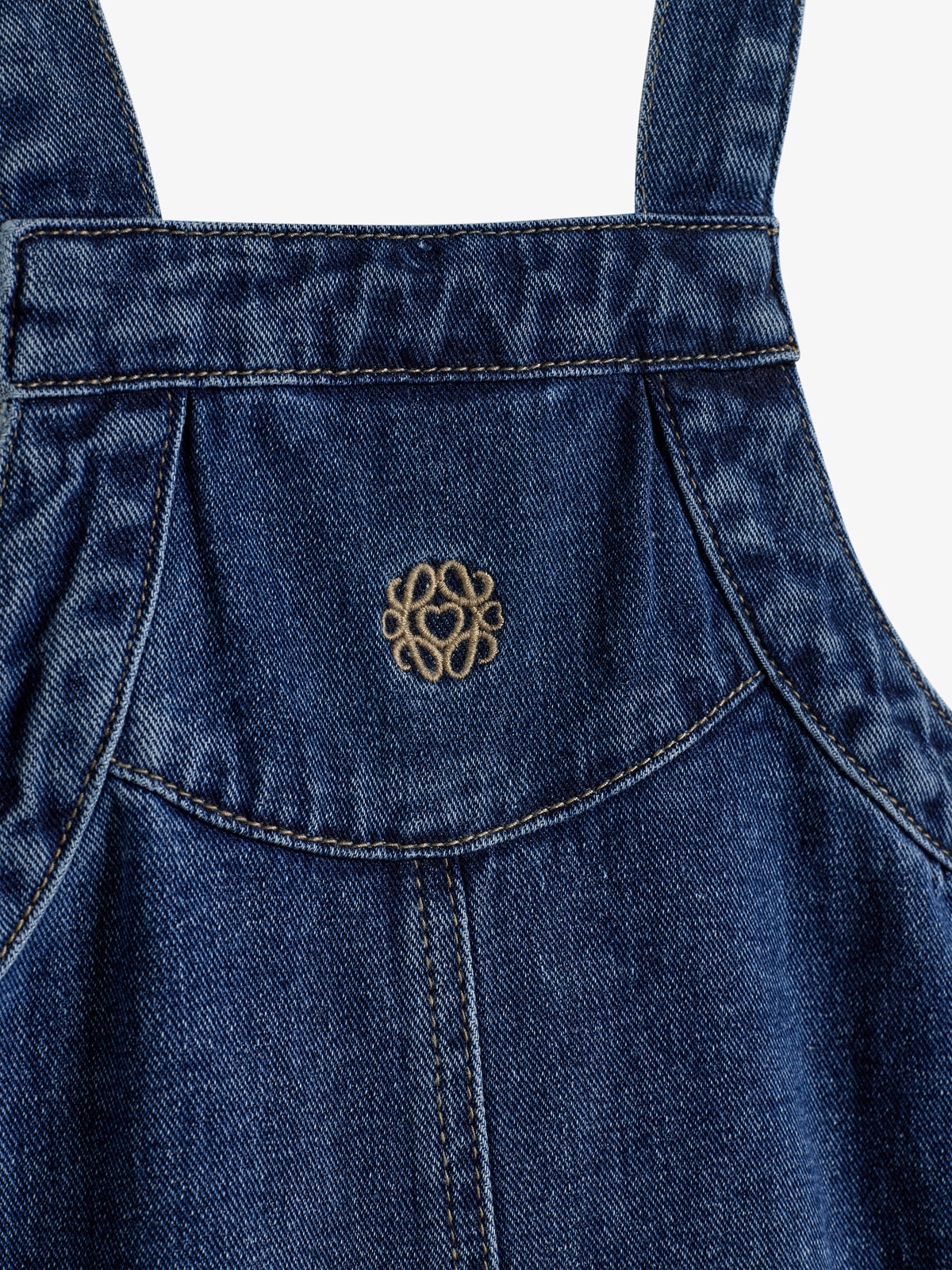 Jeansstoff-Latz zeigt eine goldene Stickerei in der Mitte und ist von Nähten umgeben. Der Stoff wirkt stabil und gut verarbeitet im Rahmen eines Kleidungsstücks.