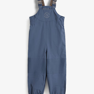 Ein blauer Kinderregenanzug mit verstellbaren Trägern liegt flach auf einem hellen Hintergrund. Text: "COMPELLOUX ADVENTURE" auf der Brust. Schwarz-graue Riemen haben Aufschrift "BY POMP DE LUX ADVENTURE".
