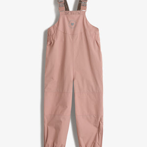 Ein rosa Kinderlatzhose mit elastischen Trägern und verstellbaren Schnallen hängt vor einem weißen Hintergrund. Auf der Brust ist ein kreisförmiges Logo mit dem Text "POLO DO LOU YAYAYAYAYAYA!".