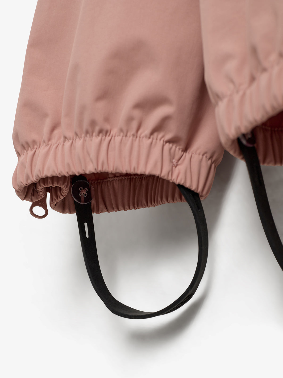 Die Jackenärmel sind aus rosa Stoff mit elastischen Bündchen, die schwarze Gummistreifen haben. Auf einem Streifen ist ein kleines Symbol sichtbar. Der Hintergrund ist weiß.