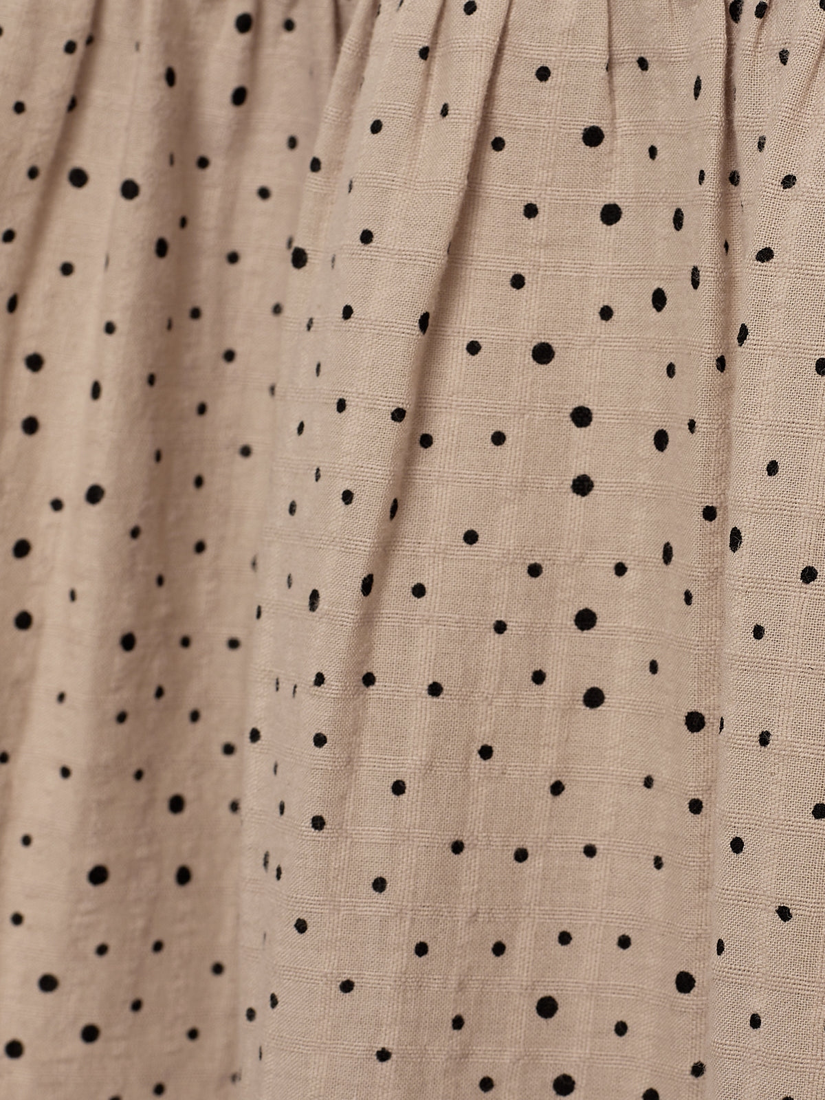 Beiger Stoff mit schwarzen Punkten, die über die glatte Oberfläche verteilt sind. Die Faltenbildung zeigt eine Textur im natürlichen Licht, die ihm ein elegantes Erscheinungsbild verleiht.