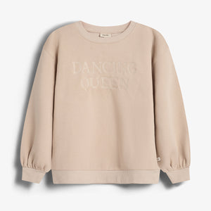Ein beige Sweatshirt mit der Aufschrift "DANCING QUEEN" in der Mitte, hängt in einem neutralen, weißen Raum. Das Sweatshirt hat lange Ärmel und gerippte Bündchen.