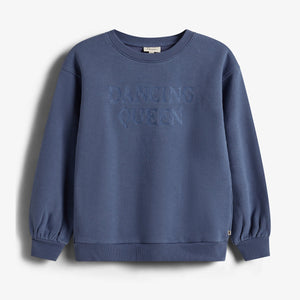 Ein blauer Pullover mit der aufgestickten Aufschrift "DANCING QUEEN" hängt vor einem weißen Hintergrund. Der Pullover hat lange Ärmel und gerippte Bündchen.