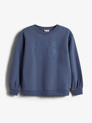 Ein blauer Pullover mit der aufgestickten Aufschrift "DANCING QUEEN" hängt vor einem weißen Hintergrund. Der Pullover hat lange Ärmel und gerippte Bündchen.