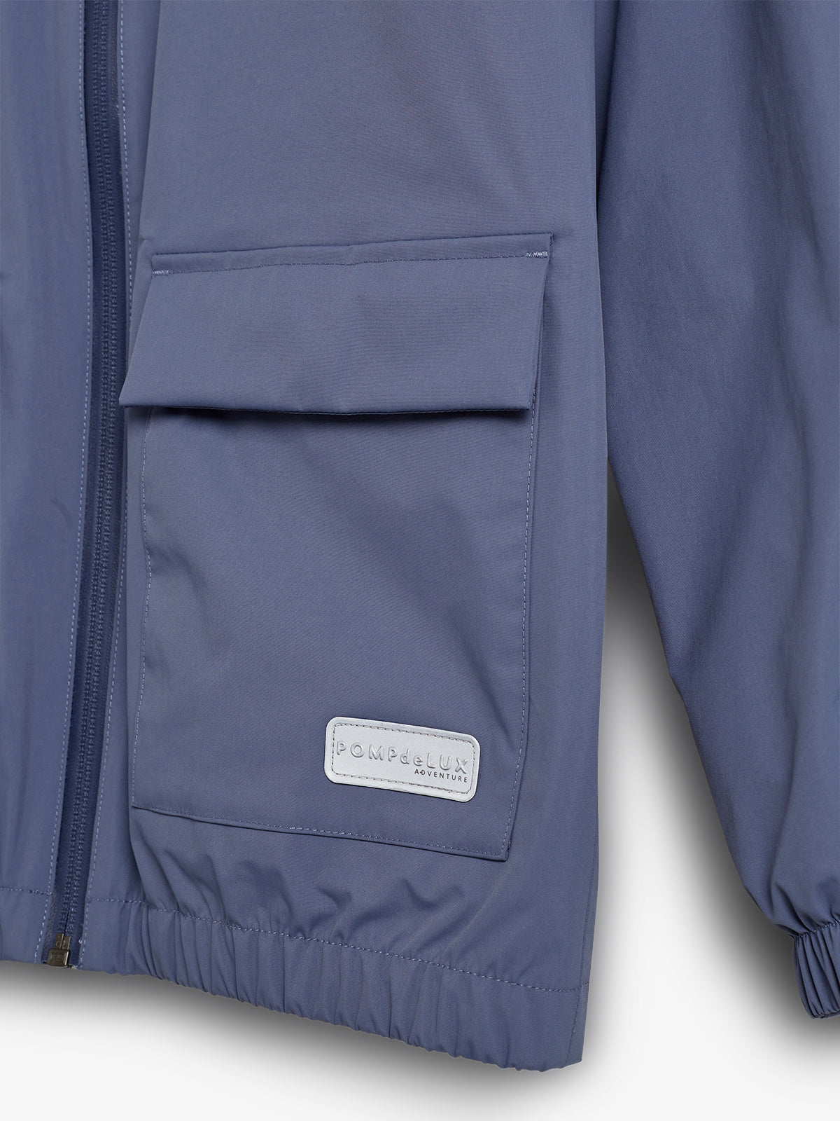 Jacke mit Reißverschluss und Tasche, trägt ein Label mit der Aufschrift "POMPdeLUX ADVENTURE". Kontext: Einfarbiger Hintergrund und elastische Bündchen.