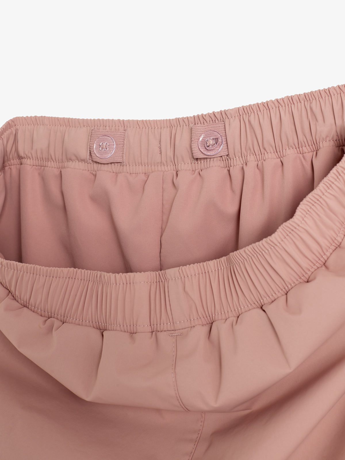 Rosa Hose mit elastischem Bund, zwei Knöpfen zur Weitenregulierung. Der Stoff ist glatt, das Bild zeigt eine Nahaufnahme der Innenseite vor einem weißen Hintergrund.