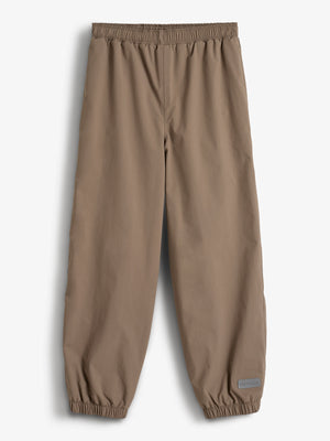 Eine braune Regenhose mit elastischem Bund und Beinabschlüssen liegt auf weißem Hintergrund. Unten rechts ist ein graues Etikett mit der Aufschrift „Polarn O. Pyret“ zu sehen.